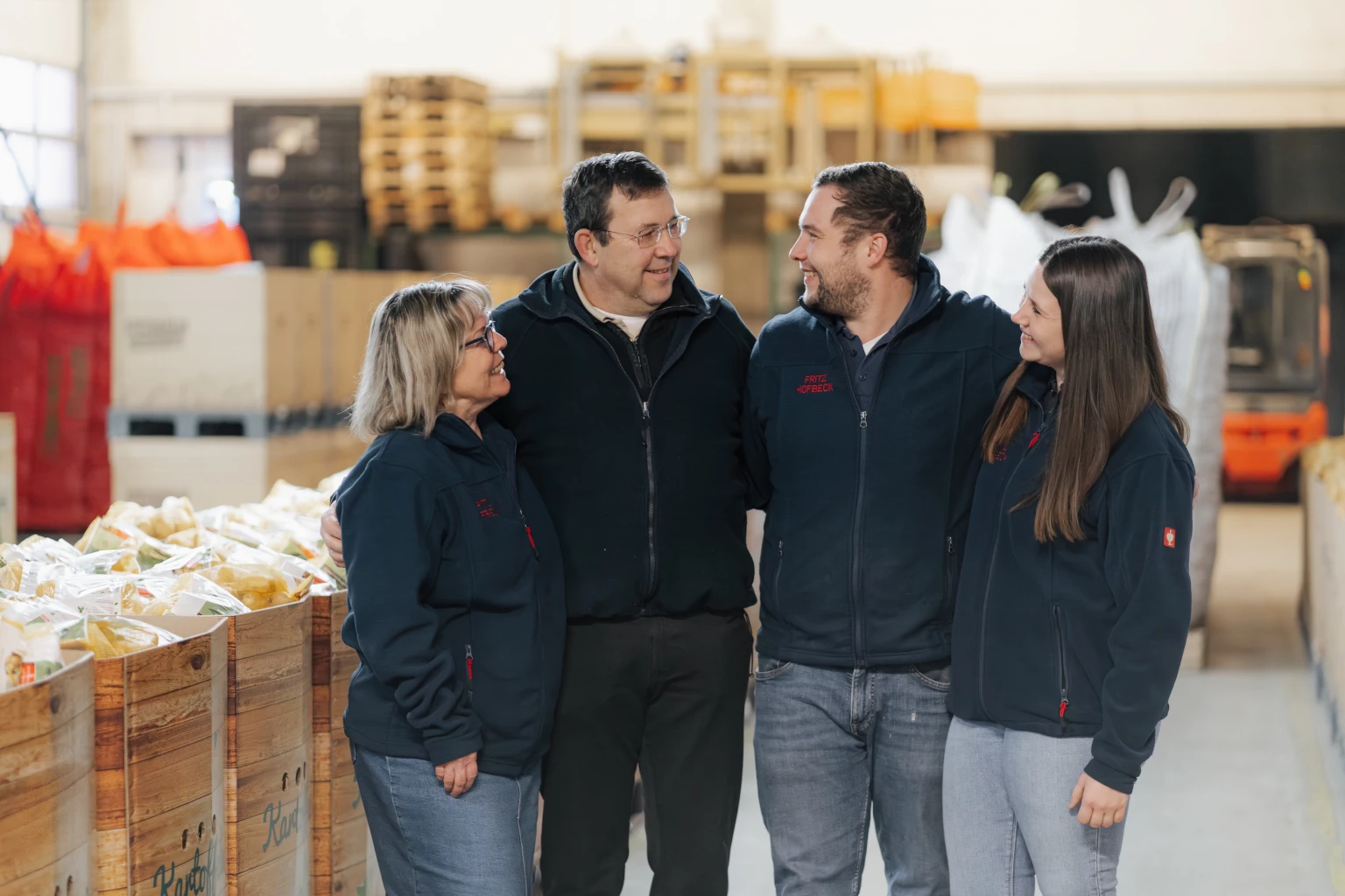Familie Hofbeck Familie Hofbeck steht gemeinsam im Betrieb von Fritz Hofbeck zwischen verpackten Kartoffeln und Arbeitsbereichen.